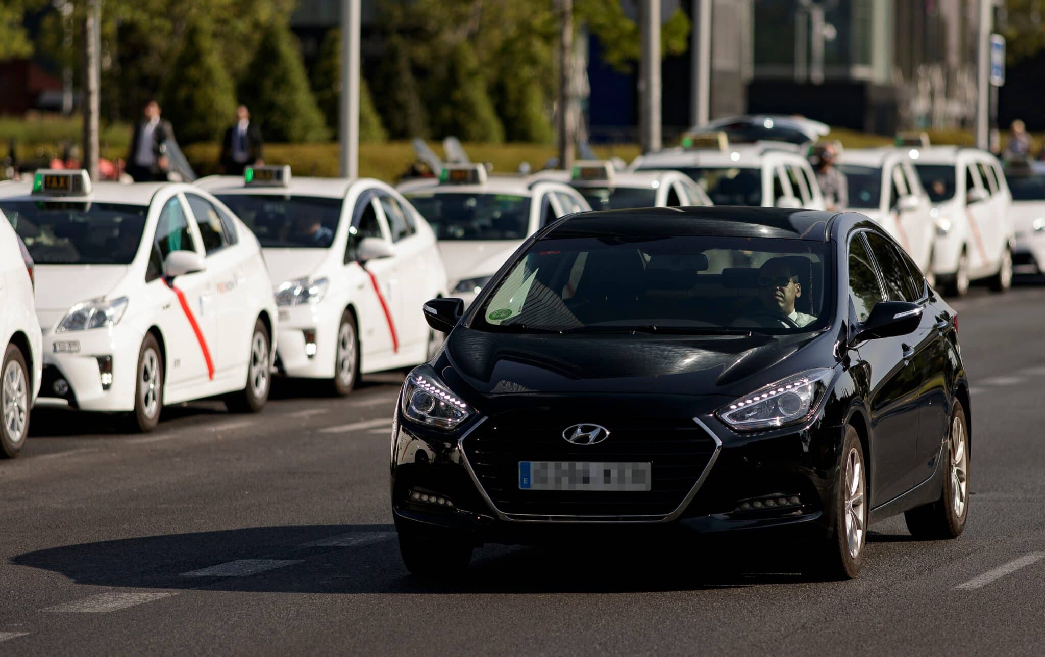 Vehículo VTC circula ante una fila de taxis en el centro de Madrid.