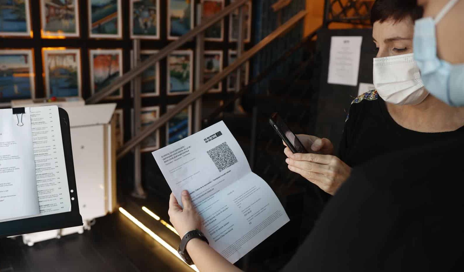 Una persona enseña el pasaporte covid a la entrada de un restaurante.