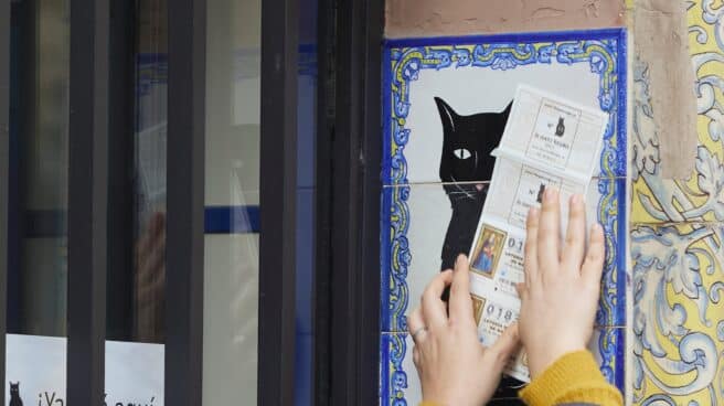 Una persona frota un billete de Lotería de Navidad por el azulejo de la Administración de Lotería el Gato Negro en Sevilla