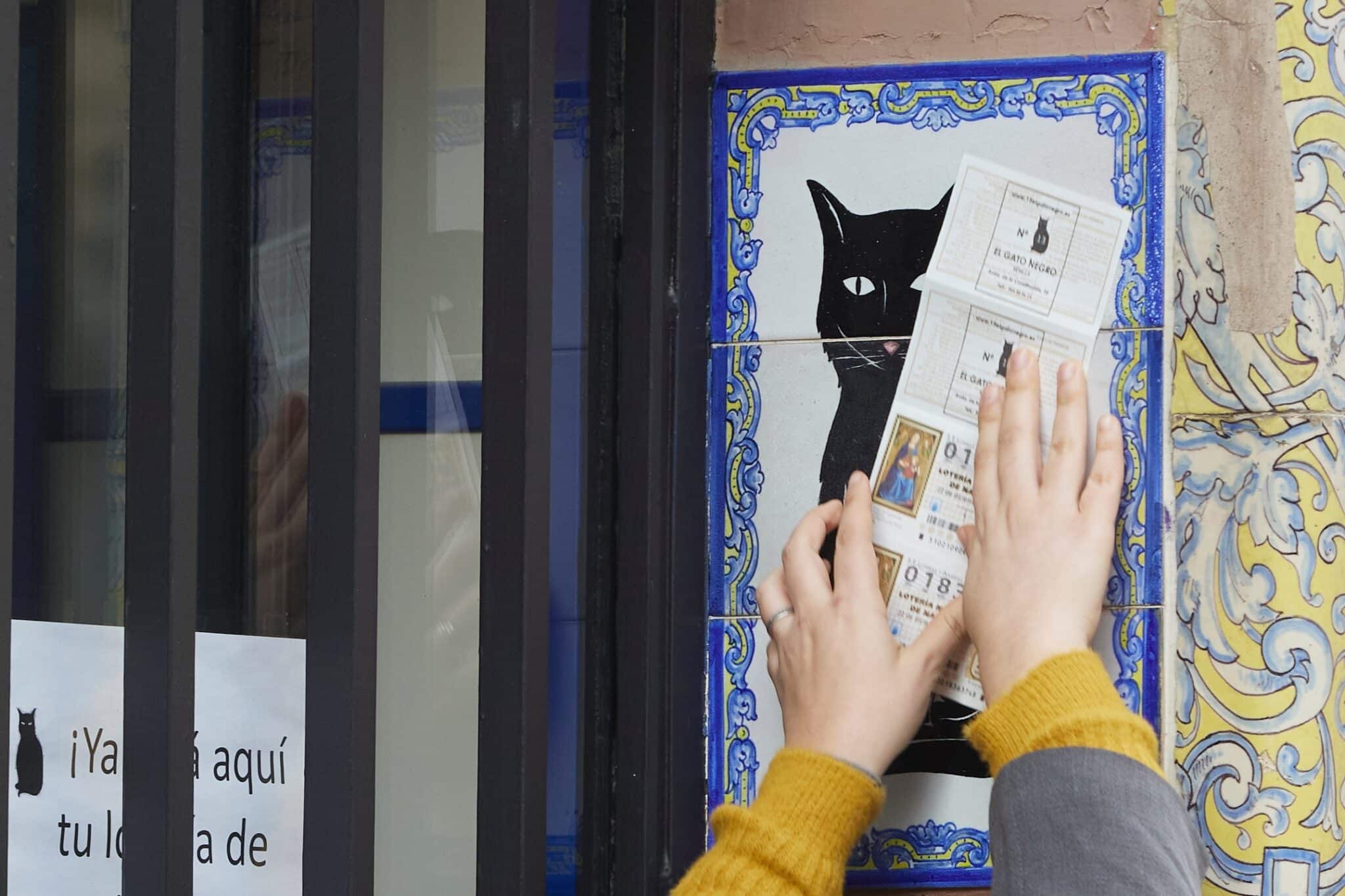 Una persona frota un billete de Lotería de Navidad por el azulejo de la Administración de Lotería el Gato Negro en Sevilla