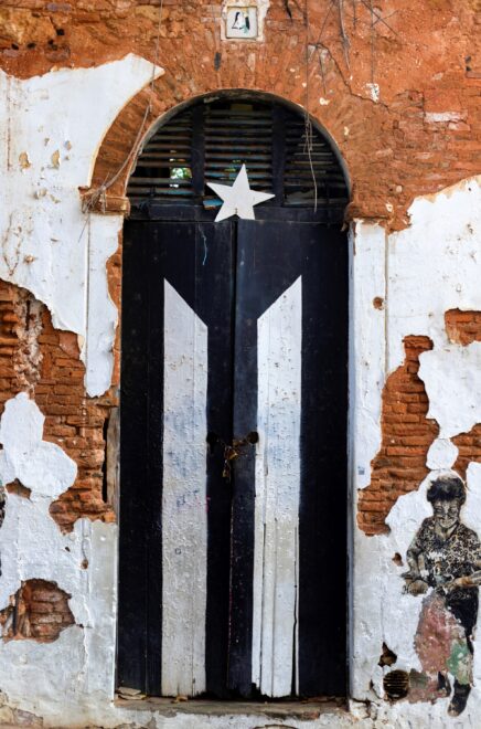 Fotografía donde se aprecia una bandera de Puerto Rico pintada en negro la puerta de una casa en ruina en la calle San José en el Viejo San Juan