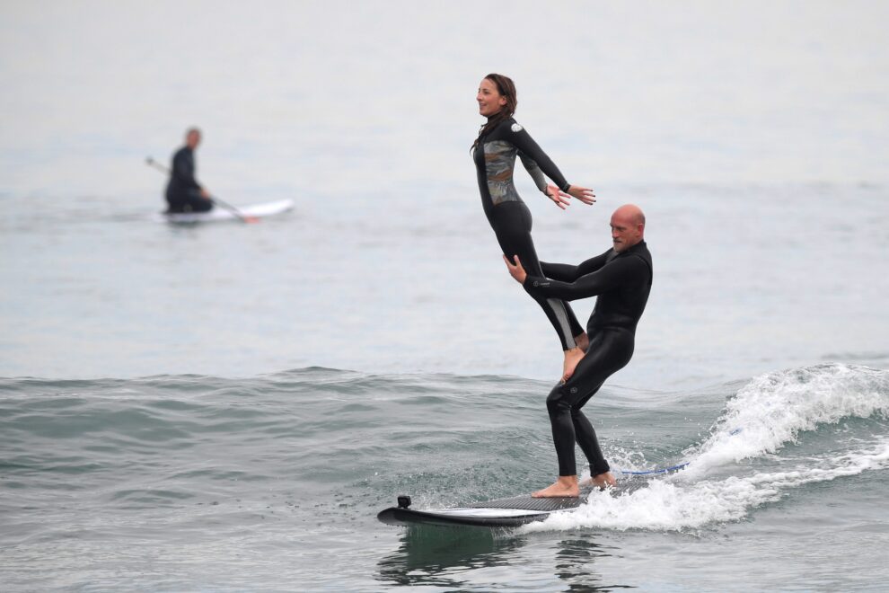Dos aficionados practican acrobacias sobre una tabla de surf en la playa de El Berrón, Asturias, este sábado, primer día del año.