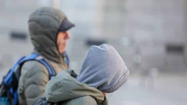 Dos jóvenes se protegen del frío y la lluvia con abrigos y gorros mientras pasean durante un día de viento por Madrid