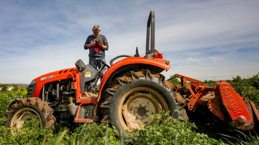 Un hombre siega la tierra del campo perteneciente a la huerta ecológica de Ecosecha, en Velilla de San Antonio, Madrid.