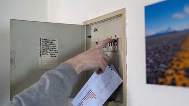 Un hombre sube los plomos de la luz con una factura de luz en la mano