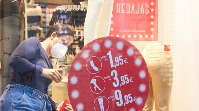 Una empleada coloca el cartel de las rebajas en una tienda de ropa.