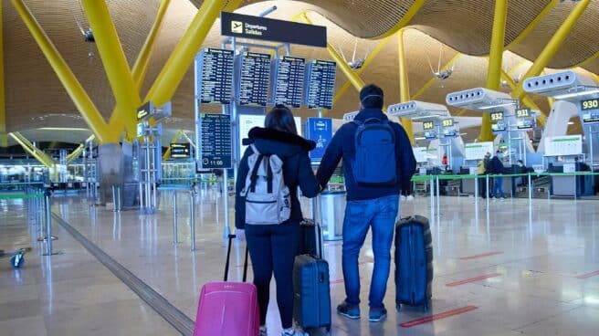 Dos viajeros miran pantallas en el aeropuerto de Barajas.