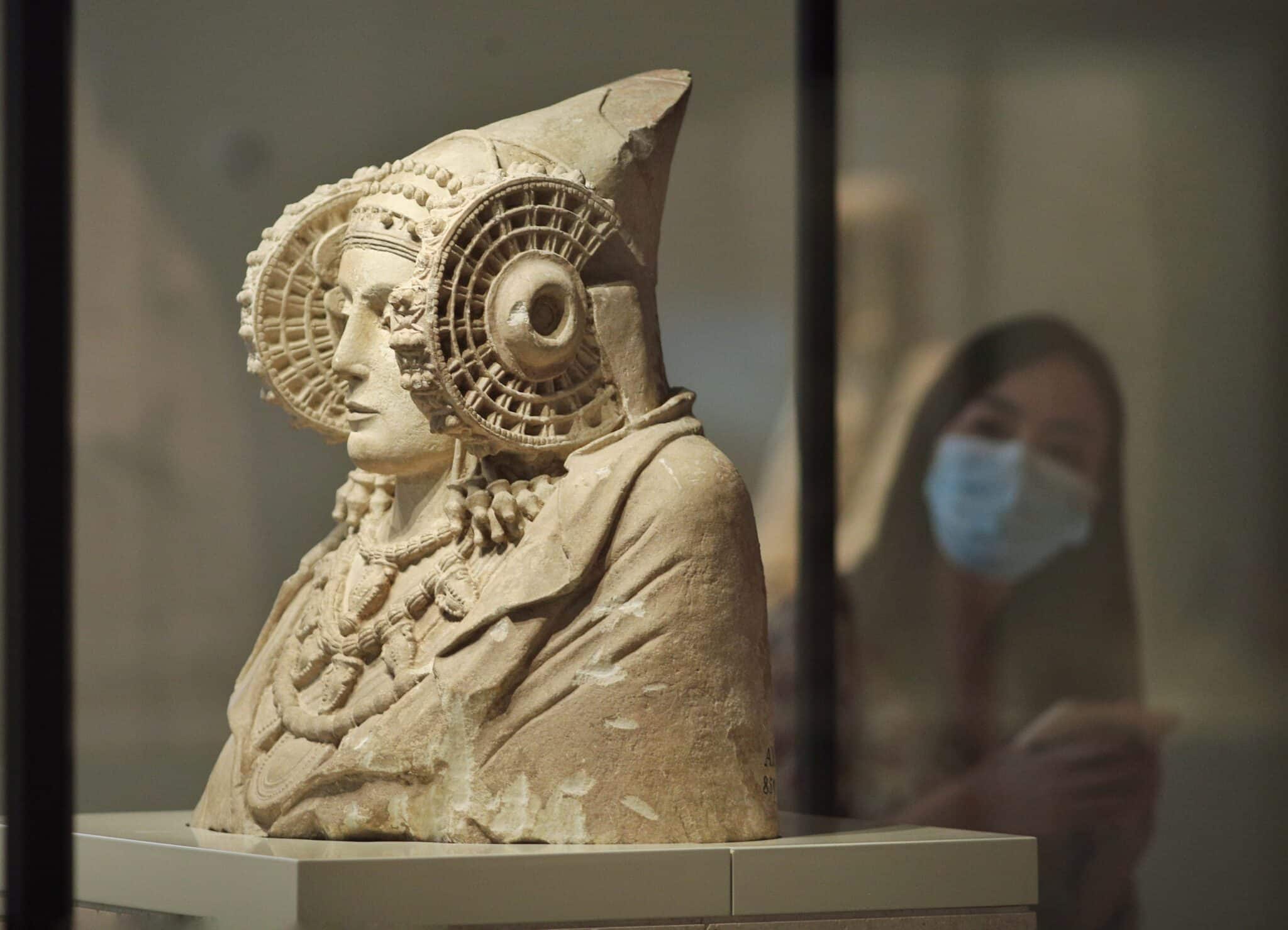 Una persona protegida con mascarilla observa la escultura de La Dama de Elche disponible en el Museo Arqueológico