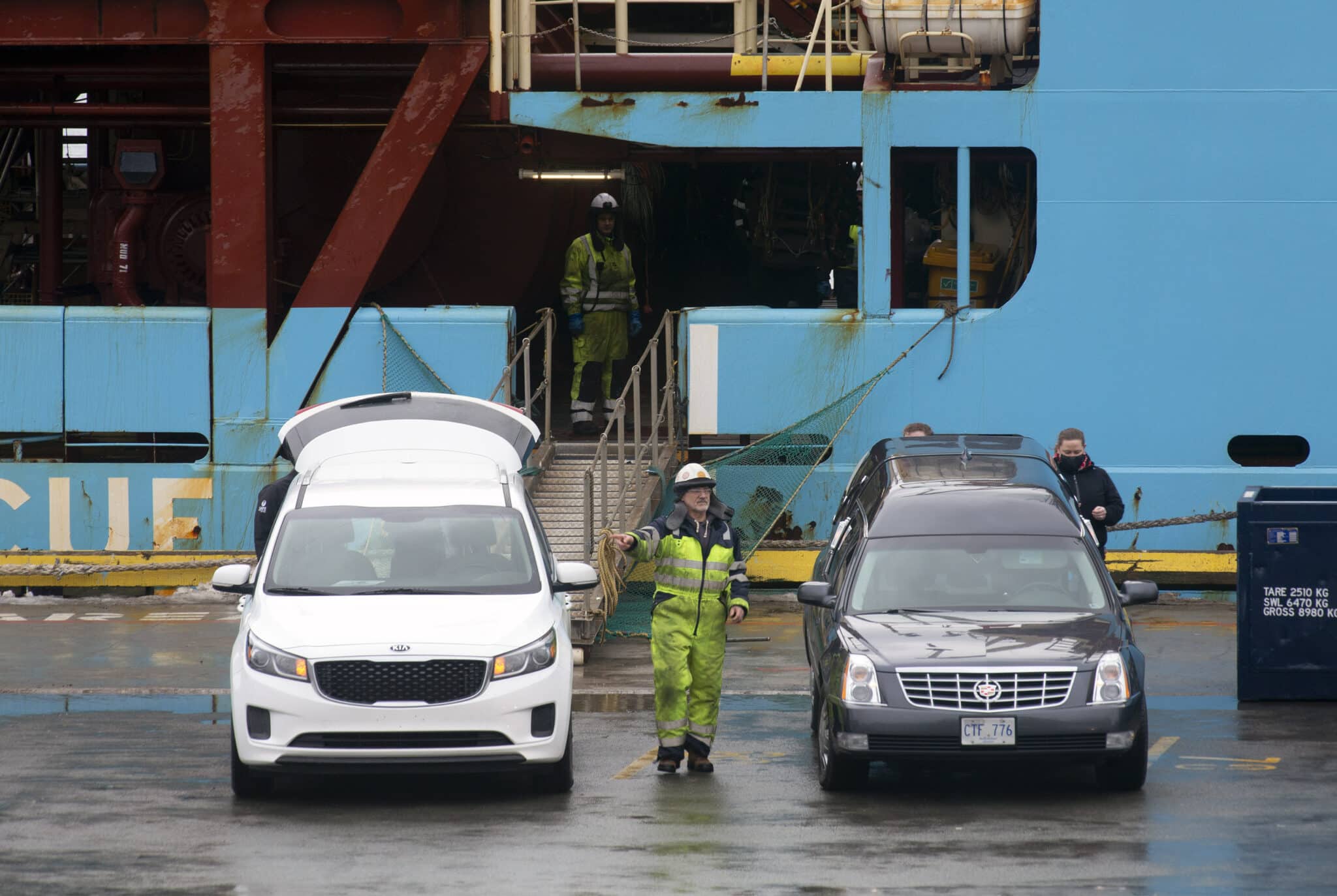 Personal portuario supervisa los coches fúnebres donde serán trasladados los cuerpos de los dos pescadores naufragados en Terranova