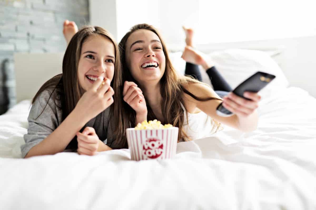 Dos chicas tumbadas sobre la cama mientras comen palomitas y ven la tv