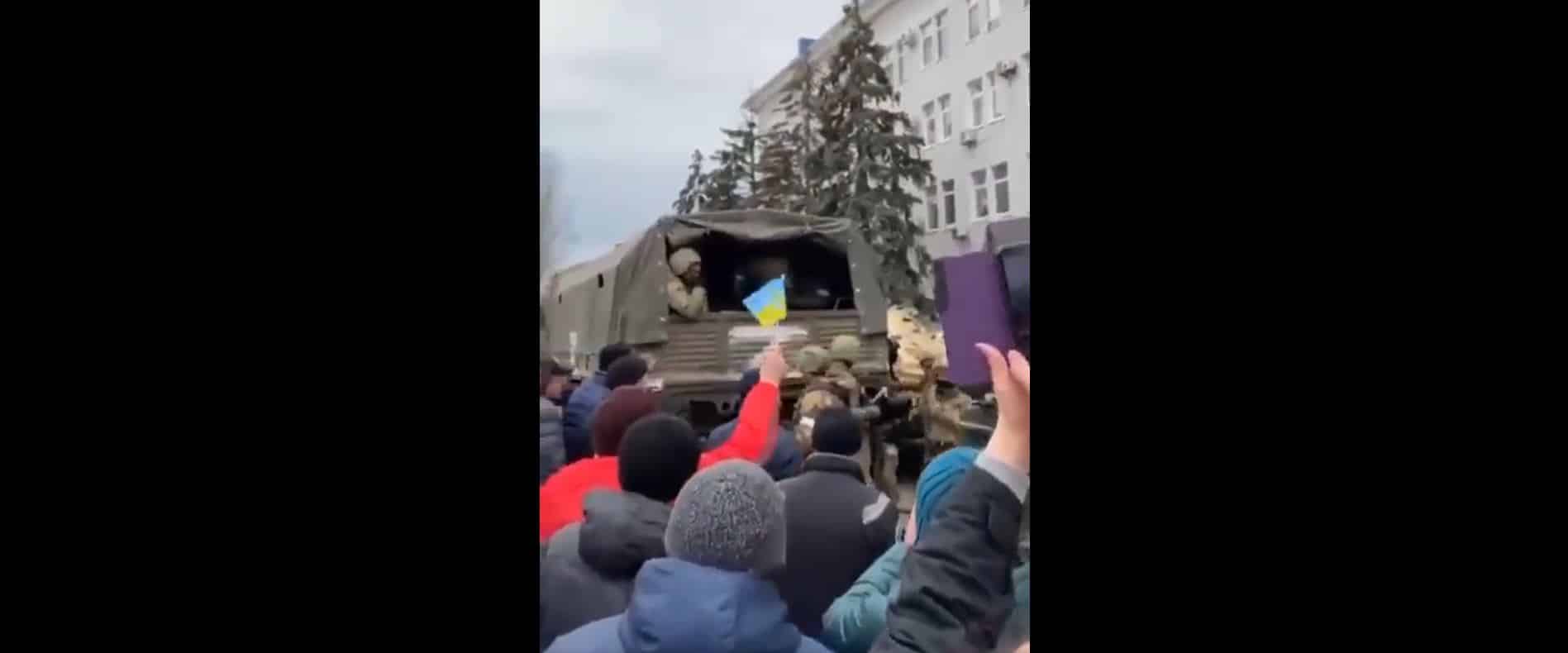 Ciudadanos muestran banderas de Ucrania y gritan contra Putin mientras los soldados rusos se montan en camiones en Berdiansk.