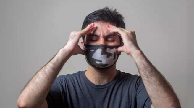 dolor-cabeza-covid Una persona con mascarilla se toca la cabeza con gesto de dolor.