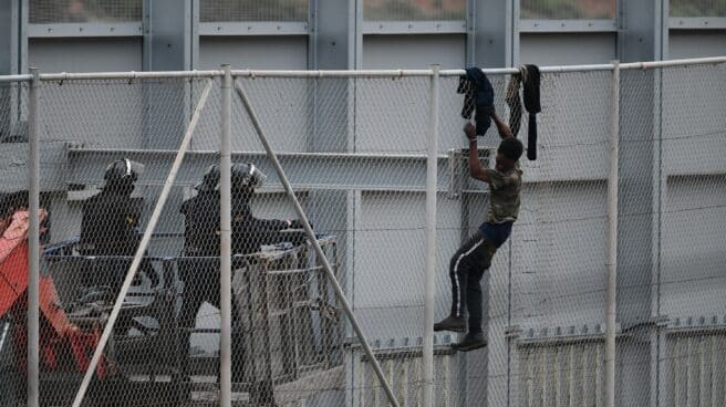 Agentes de la Guardia Civil se acercan a un migrante encaramado a la valla de Ceuta el pasado mes de abril.