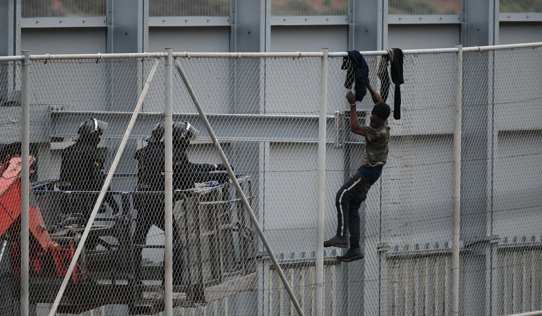 Agentes de la Guardia Civil se acercan a un migrante encaramado a la valla de Ceuta el pasado mes de abril.