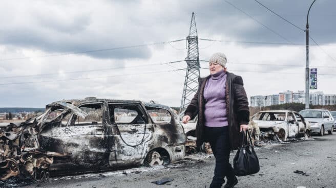 Una mujer camina delante de unos coches quemados en un puente de Irpin (Ucrania)