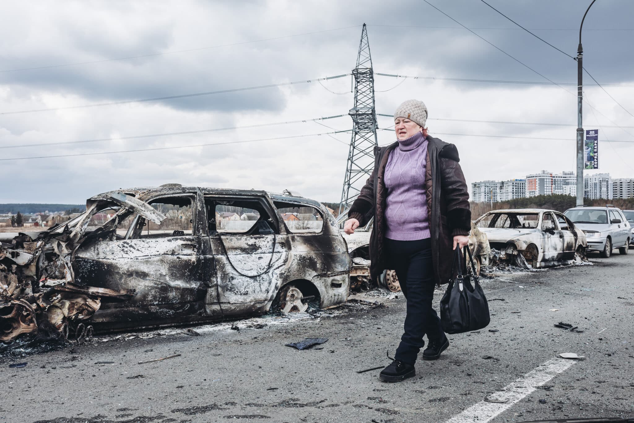 Una mujer camina delante de unos coches quemados en un puente de Irpin (Ucrania)