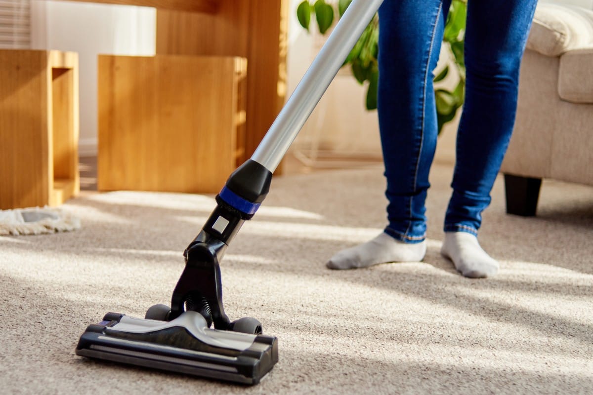Aspiradora sin cables sobre alfombra y los pies descalzos de la persona que aspira