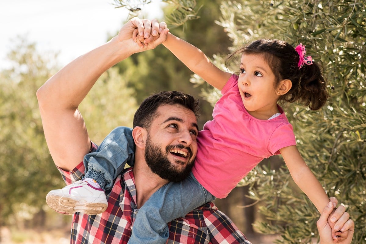 Hombre con una niña sobre los hombros y los brazos extendidos