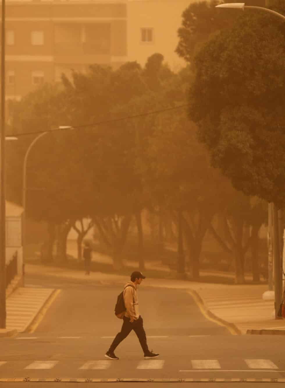 Persona cruzando la calle de Almería cubierta de polvo rojo por la calima