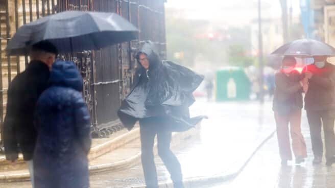 Gente anda por la calle en Málaga mientras llueve intensamente.