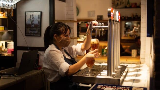 Una camarera sirve una cerveza en el interior de un bar en una calle céntrica de Barcelona.