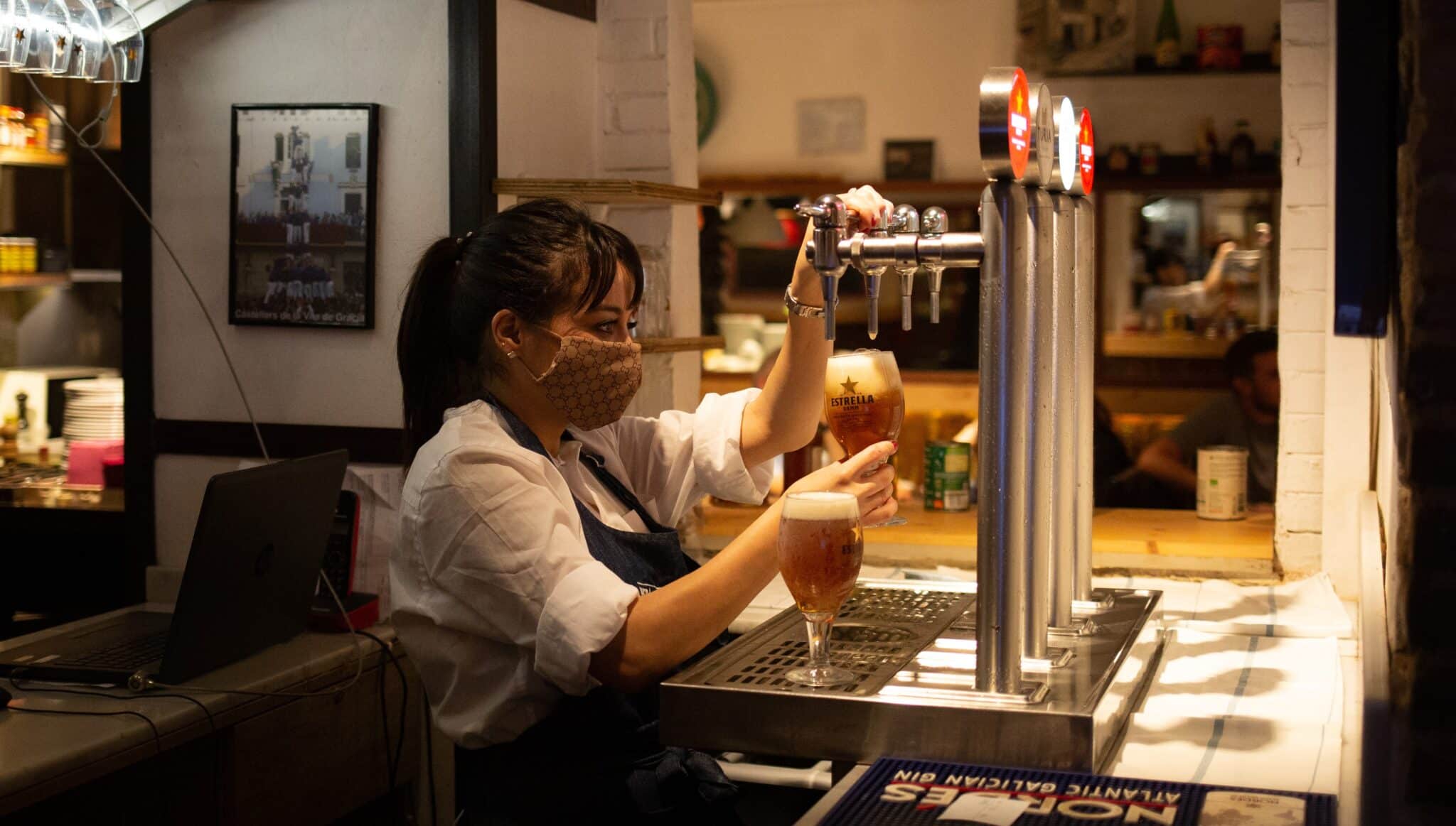 Una camarera sirve una cerveza en el interior de un bar en una calle céntrica de Barcelona.