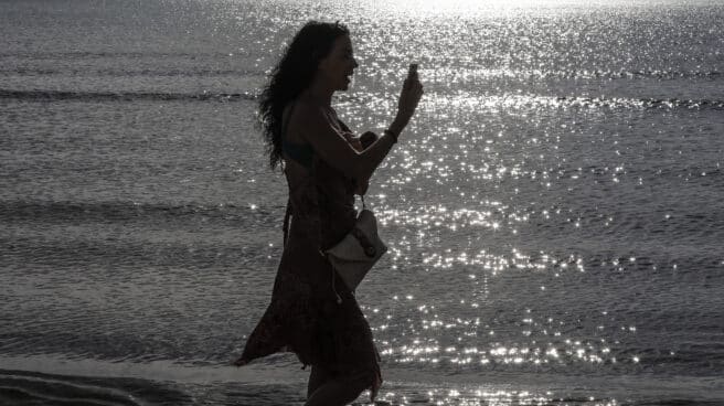 Una mujer pasea durante esta Semana Santa por la playa con su teléfono móvil