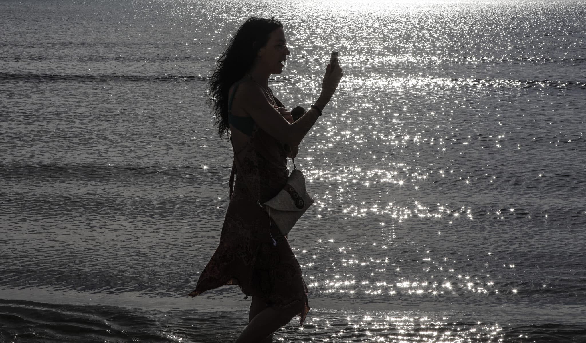 Una mujer pasea durante esta Semana Santa por la playa con su teléfono móvil