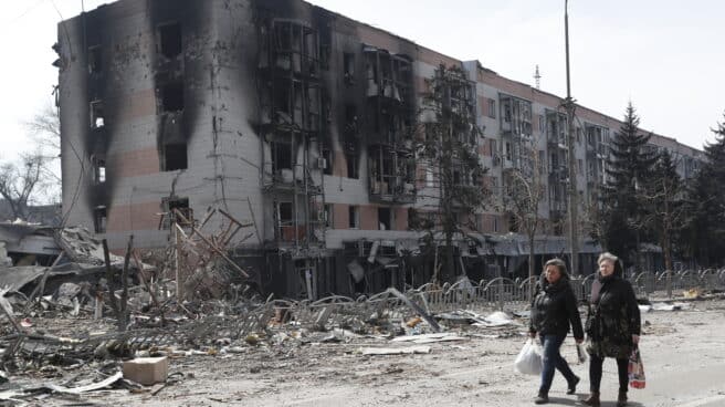 Dos mujeres caminan frente a un edificio destruido en Mariúpol.
