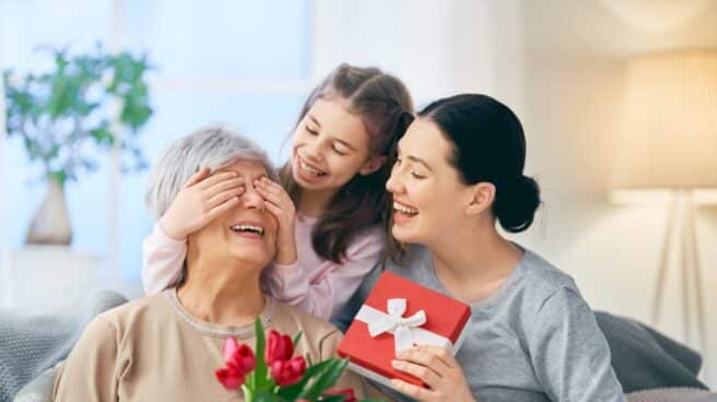 Dos mujeres de diferentes edades y una niña sonrientes entre ramos de flores y regalos