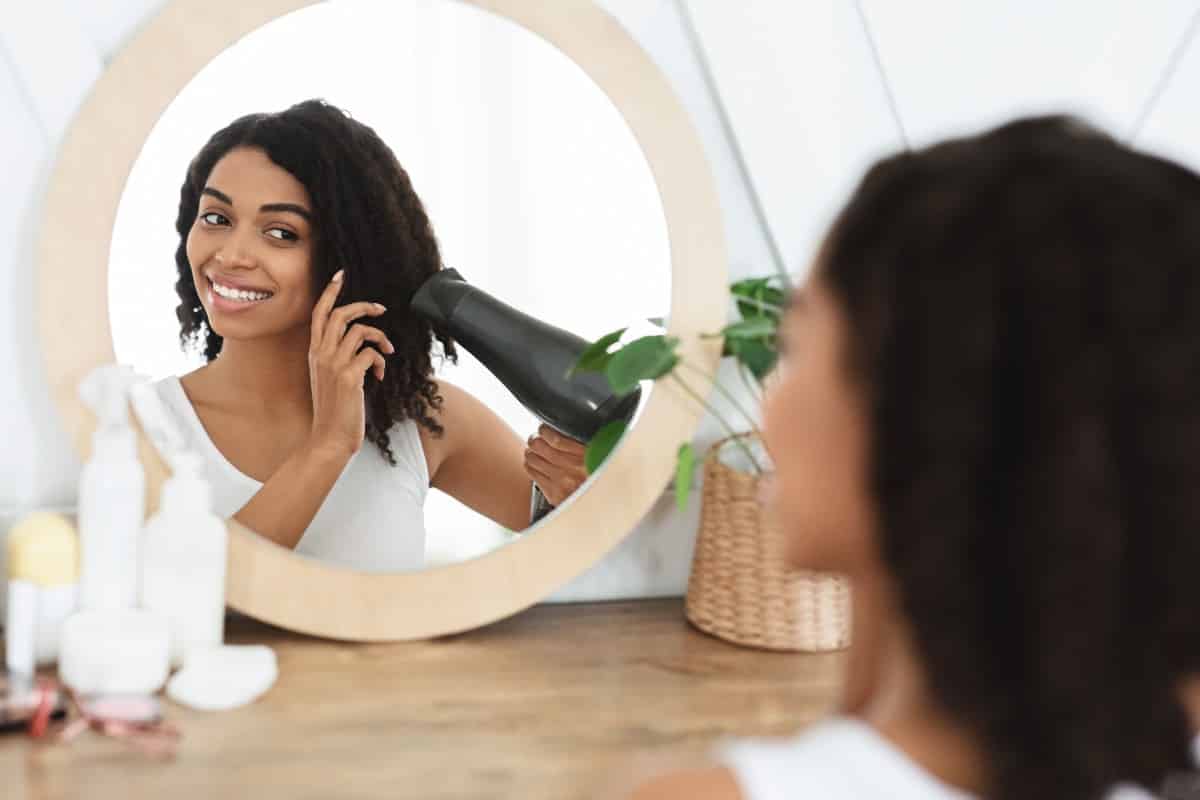 Chica mirando al espejo mientras se seca con un secador