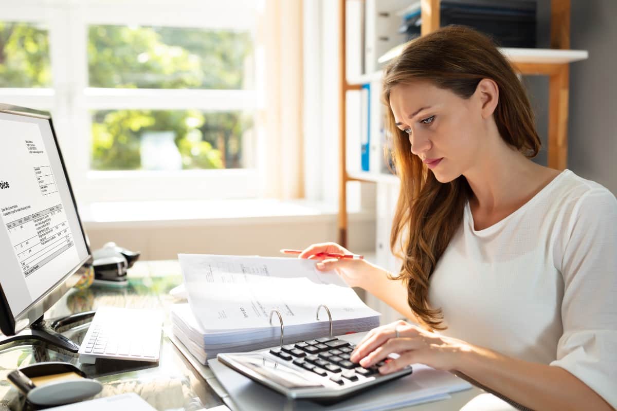 Mujer en escritorio frente a un ordenador, papeles y calculadora, preparando la declaración de la renta
