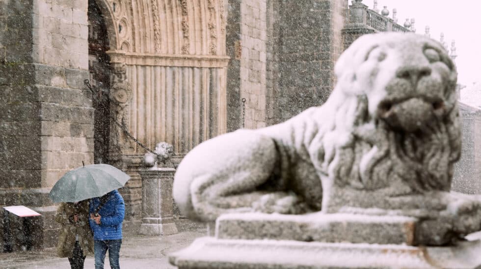 Dos personas se protegen de la nieve junto a los leones de la catedral de Ávila