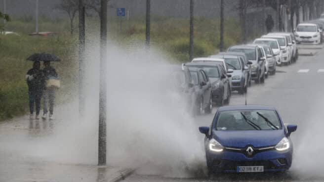 Un vehículo levanta el agua acumulada cuando el cielo de la Comunitat Valenciana permanecerá este martes nuboso o cubierto