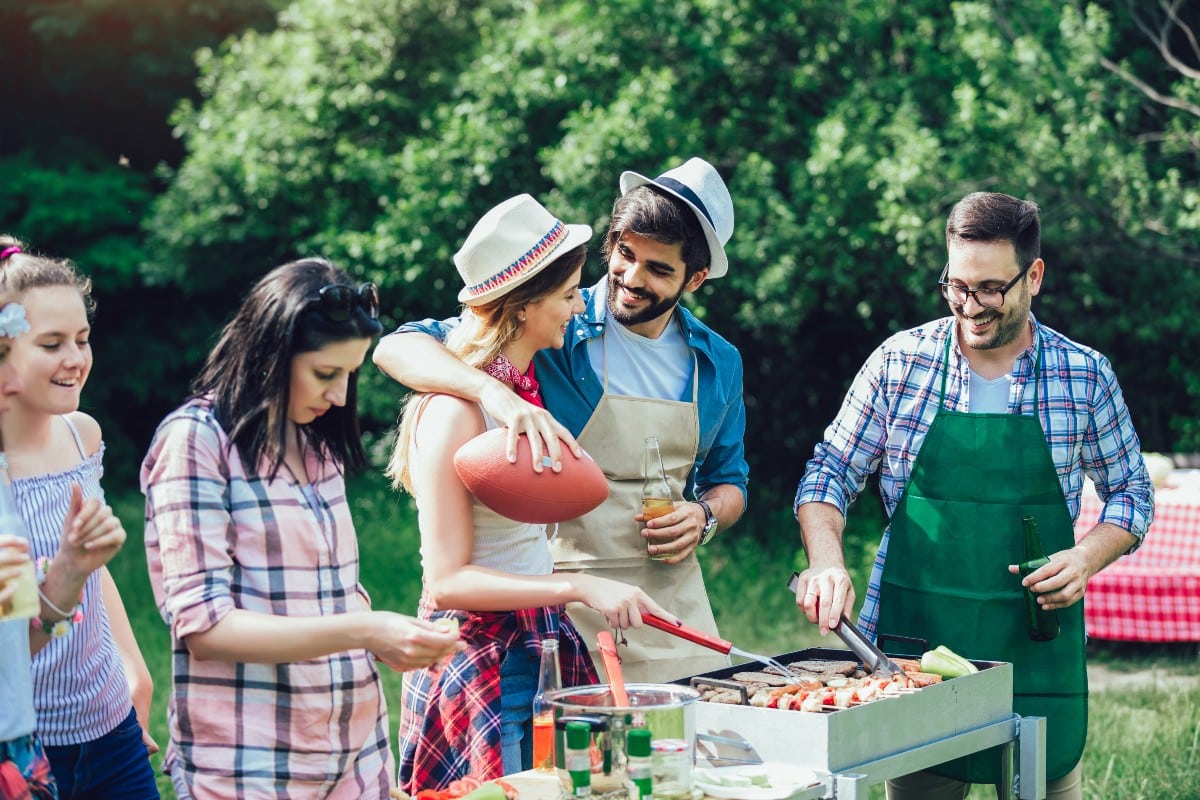 Cinco personas alrededor de una barbacoa mientras los alimentos se cocinas