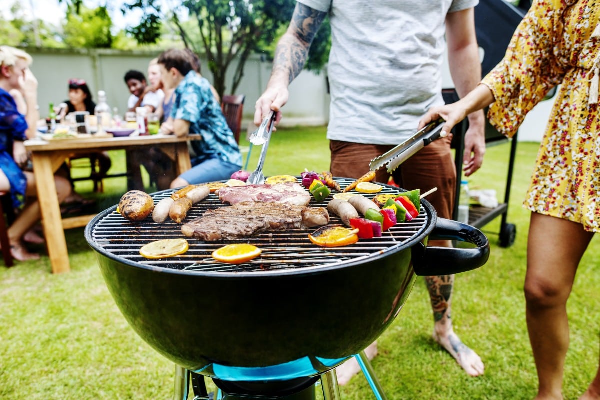 Grupo de personas alrededor de una barbacoa negra con alimentos en la superficie