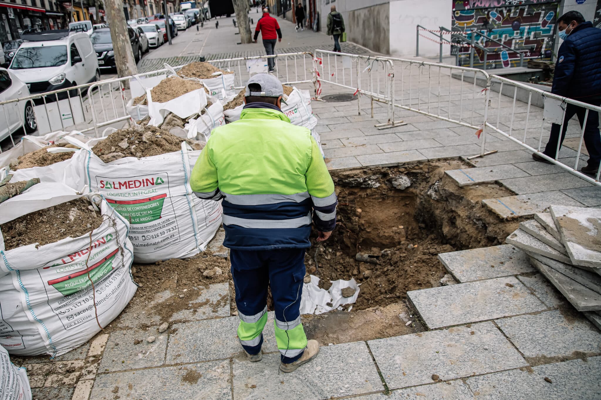 Un obrero junto a unos sacos de tierra en una obra de una acera, en el centro de Madrid.