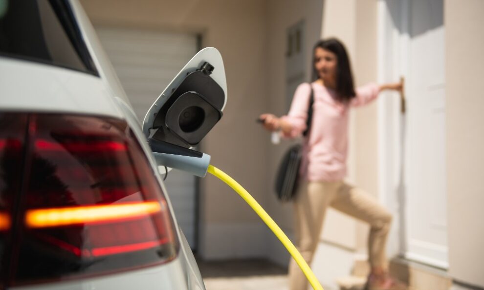 Coche eléctrico cargándose con una mujer conductora detrás