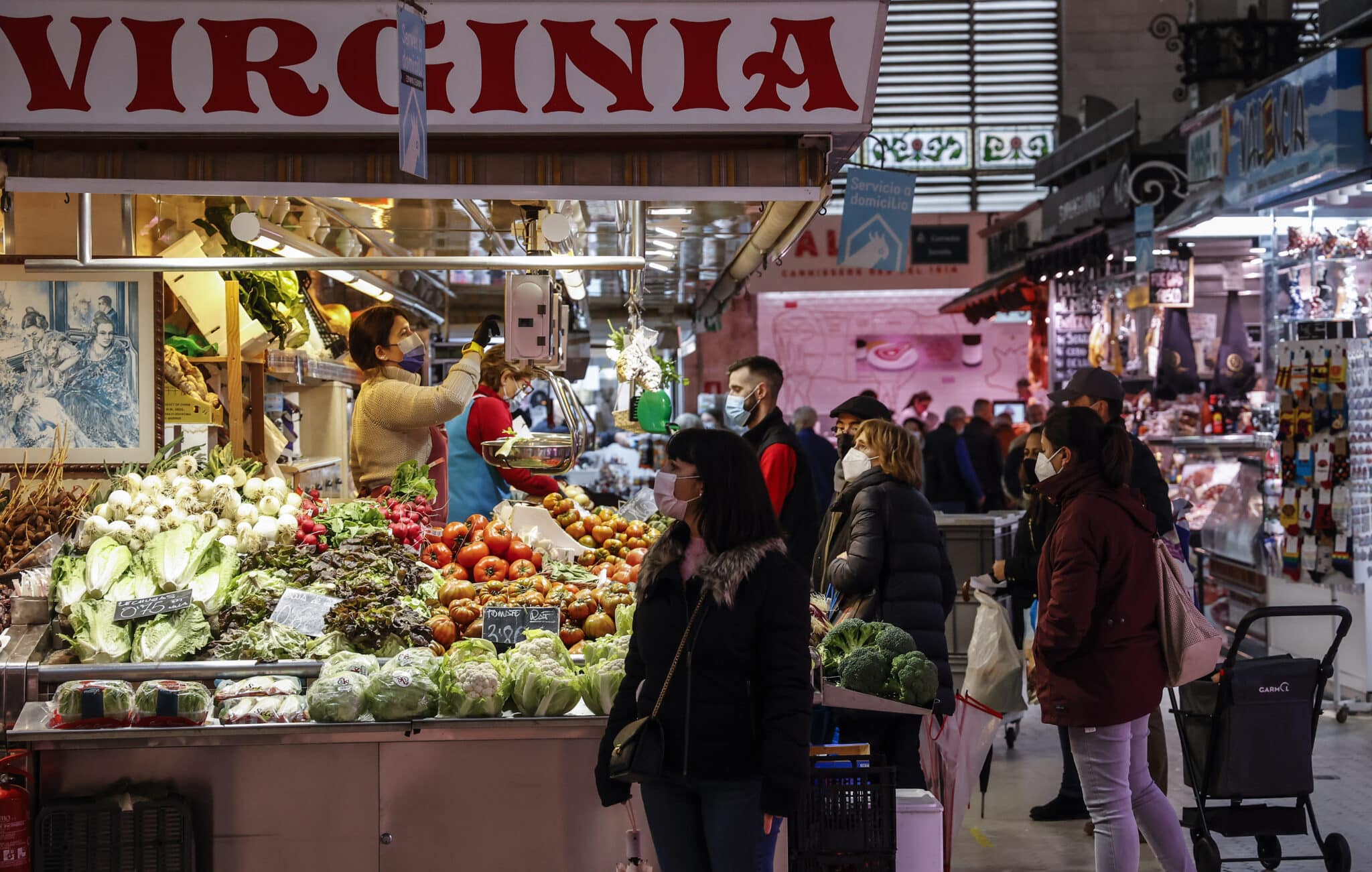 Varias personas compran en un puesto de fruta y verdura en el Mercado Central de Valencia.