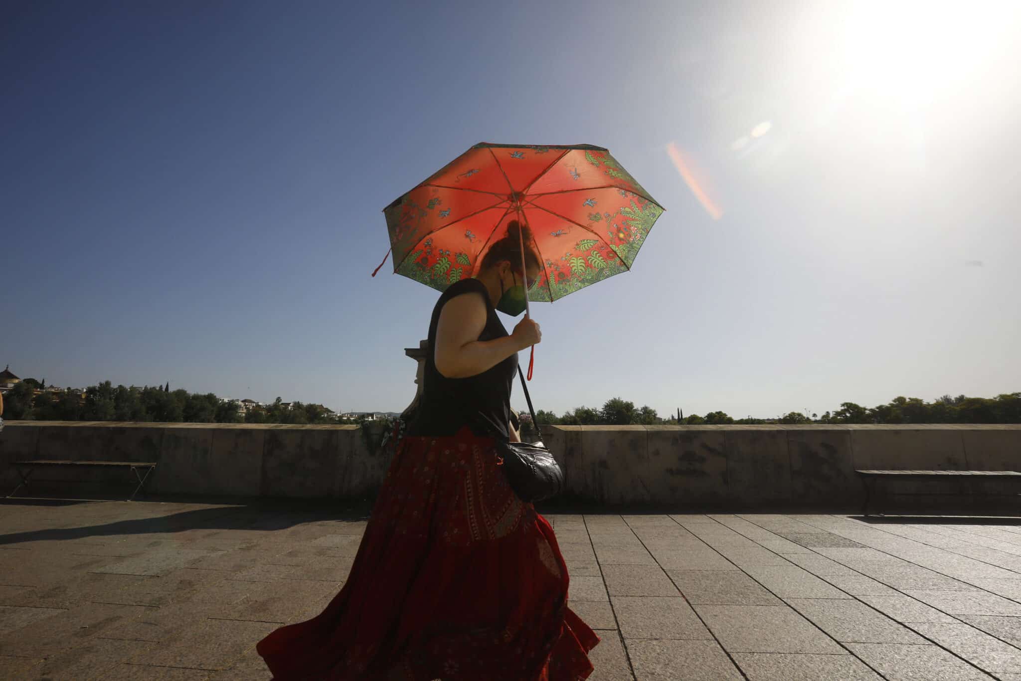 Una mujer se protege con un paraguas de las altas temperaturas mientras pasea por el puente Romano de Córdoba