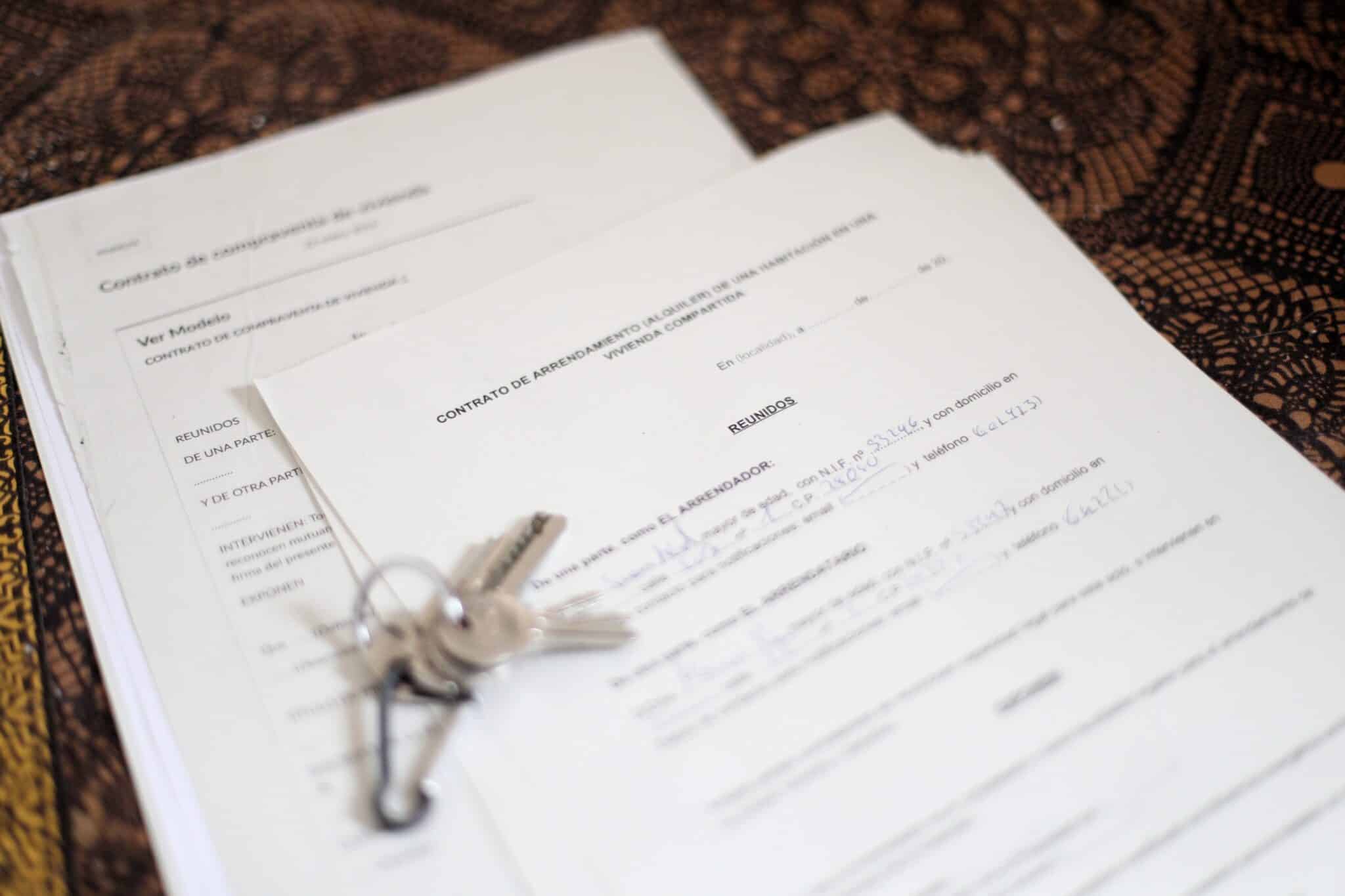 Unas llaves sobre un contrato de compraventa de vivienda y un contrato de alquiler de una habitación en una vivienda compartida.