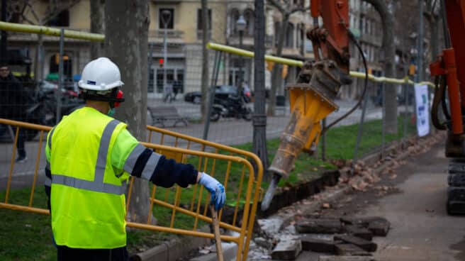 Un obrero y una máquina excavadora trabajan en las obras para unir el tranvía por la Diagonal (Barcelona).