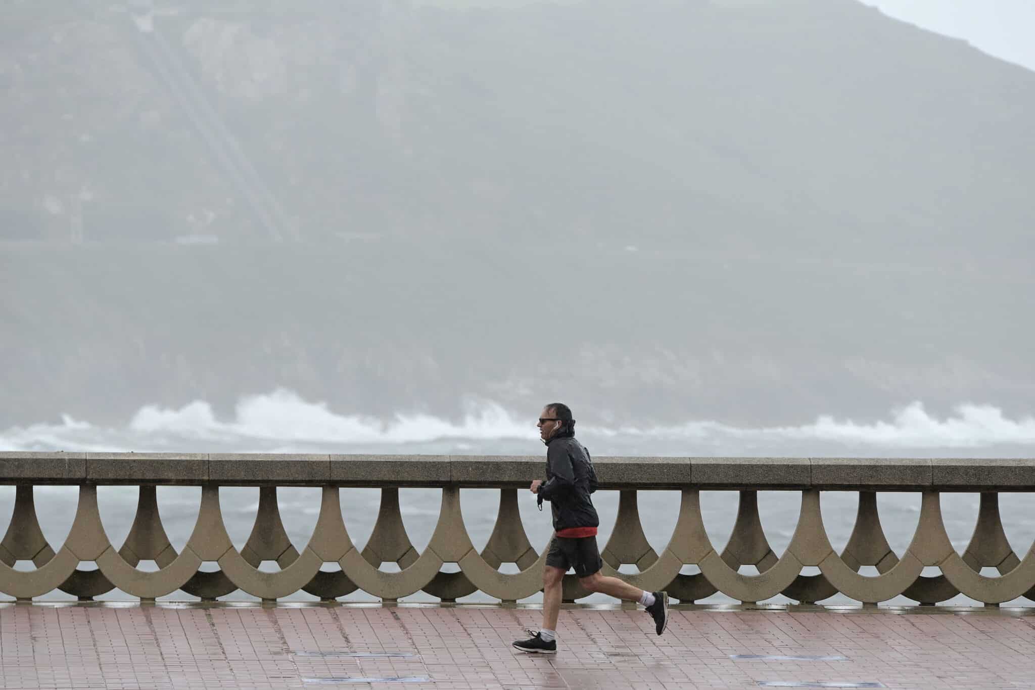 Un hombre, con chubasquero, corre por el Paseo Marítimo de La Coruña