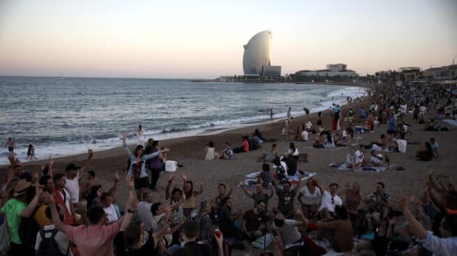 Un grupo de personas sentadas en la arena de la playa durante la tradicional verbena de Sant Joan