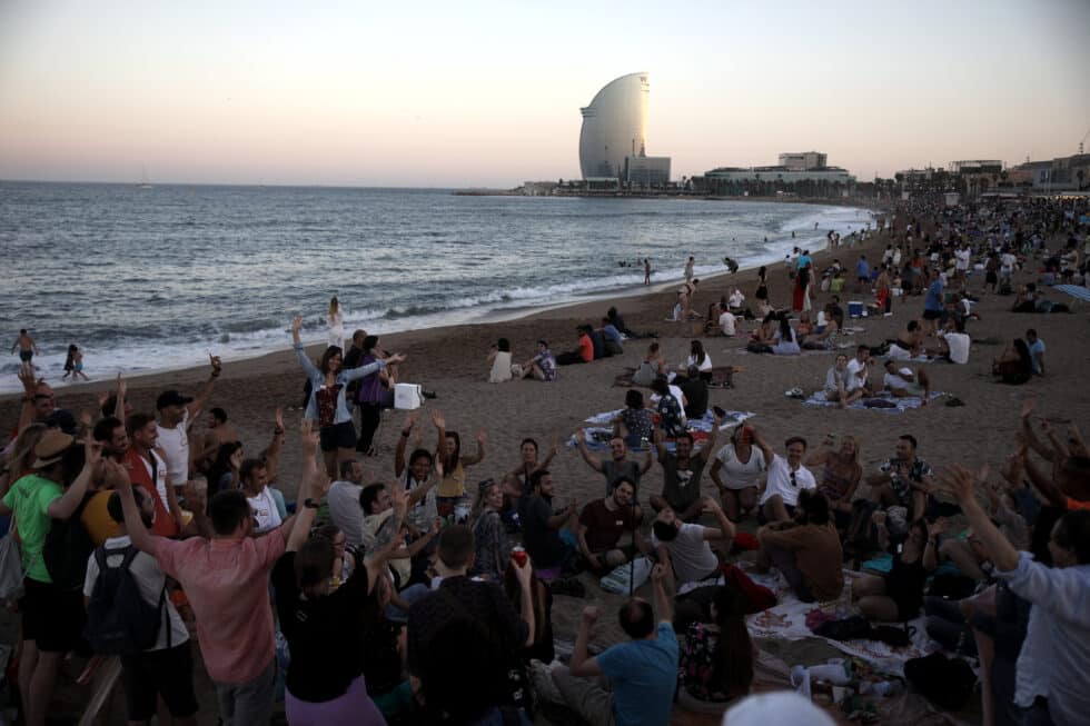 Un grupo de personas sentadas en la arena de la playa durante la tradicional verbena de Sant Joan