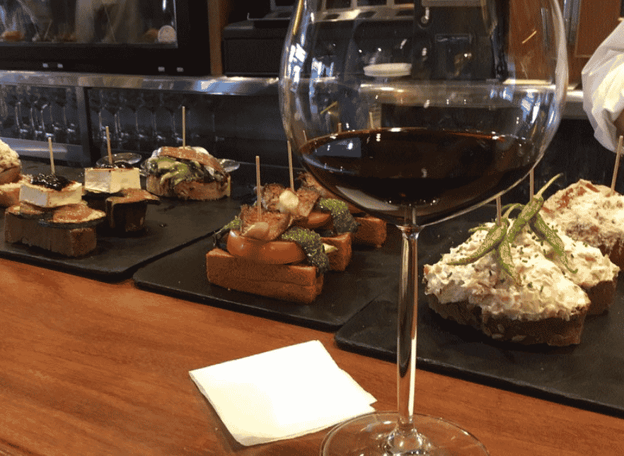 Tapas en una barra junto a una copa de vino en el bar Mugi, en Bilbao