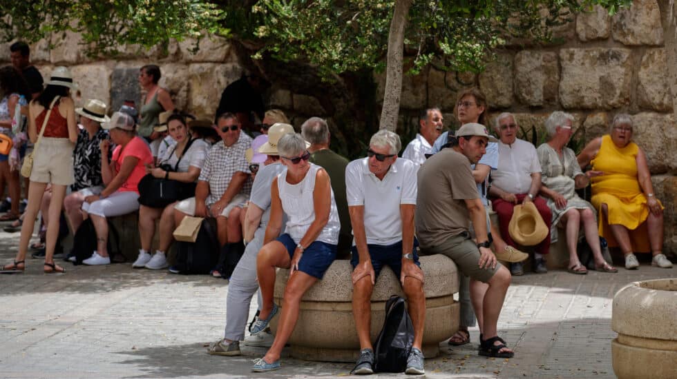 Unos turistas descansan sentados a la sombra junto a los Reales Alcázares de Sevilla