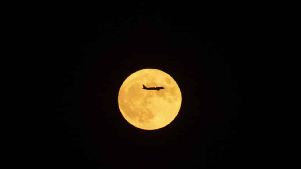 Un avión en dirección al aeropuerto del Prat pasa por delante de la primera luna llena de verano esta noche sobre el cielo de Barcelona.