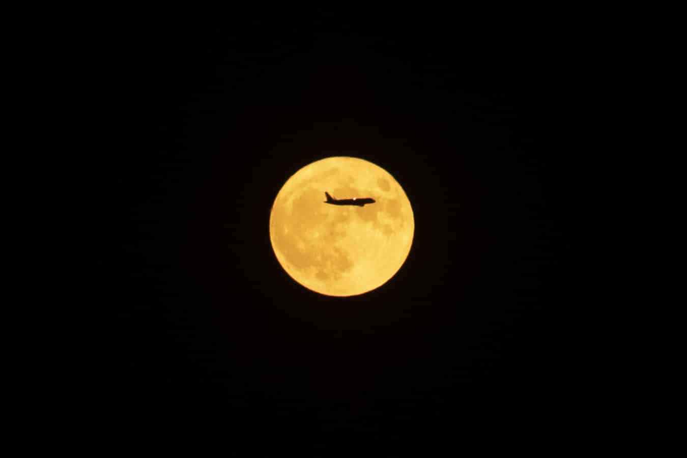 Un avión en dirección al aeropuerto del Prat pasa por delante de la primera luna llena de verano esta noche sobre el cielo de Barcelona.