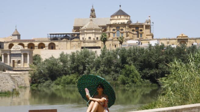 Una turista se protege del calor con un paraguas y un abanico a la orilla del río Guadalquivir cerca de la Mezquita-Catedral de Córdoba ( al fondo) hoy lunes cuando la Agencia Estatal de Meteorología (Aemet),